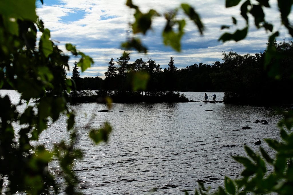 barefoot bride and groom carefully crossing rocks in Calabogie lake