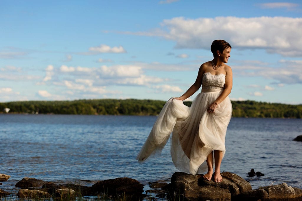 barefoot bride holding dress and standing on rock in Calabogie lake
