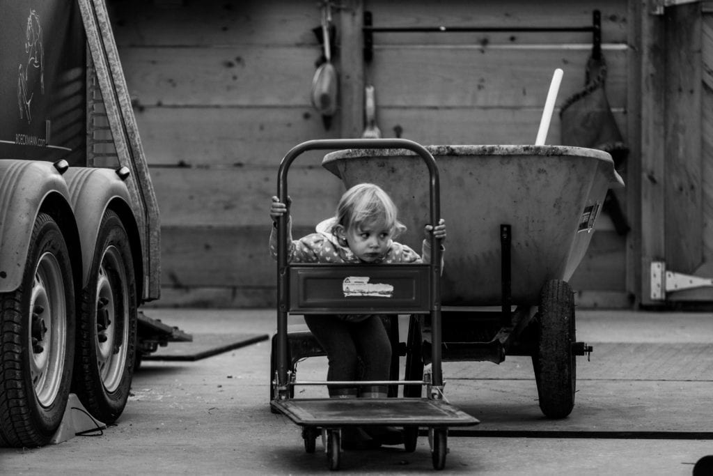 little girl peeking through cart at horse stable