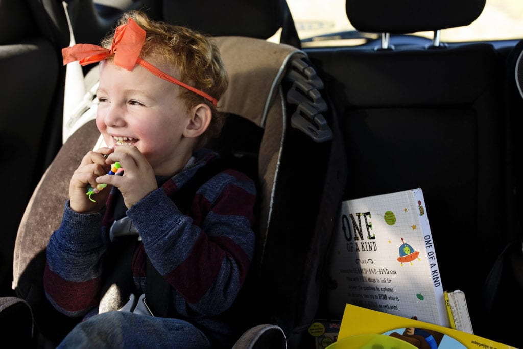little boy in back seat wearing silly headband and laughing looking out the window