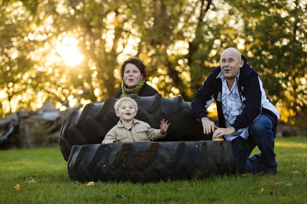 mom and dad playing in tractor tires with young blonde boy rural family shoot