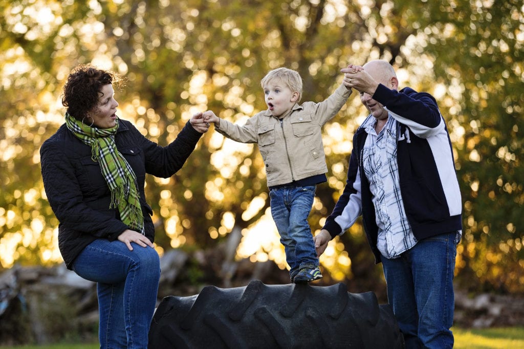 son playing with parents on tractor tires in rural fall family session