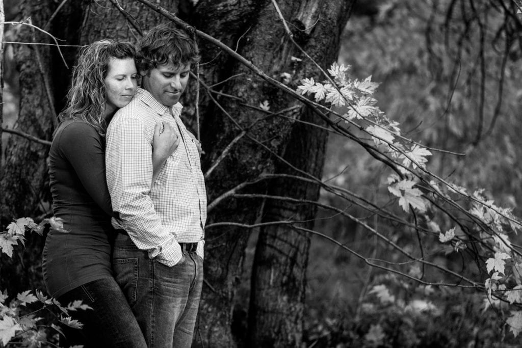 woman embracing fiance beside large tree in black and white fall engagement photo