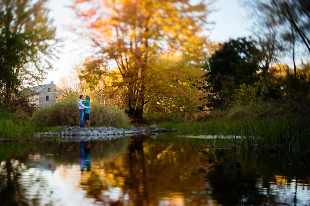 Couple standing beside reflection in water with fall trees and mill