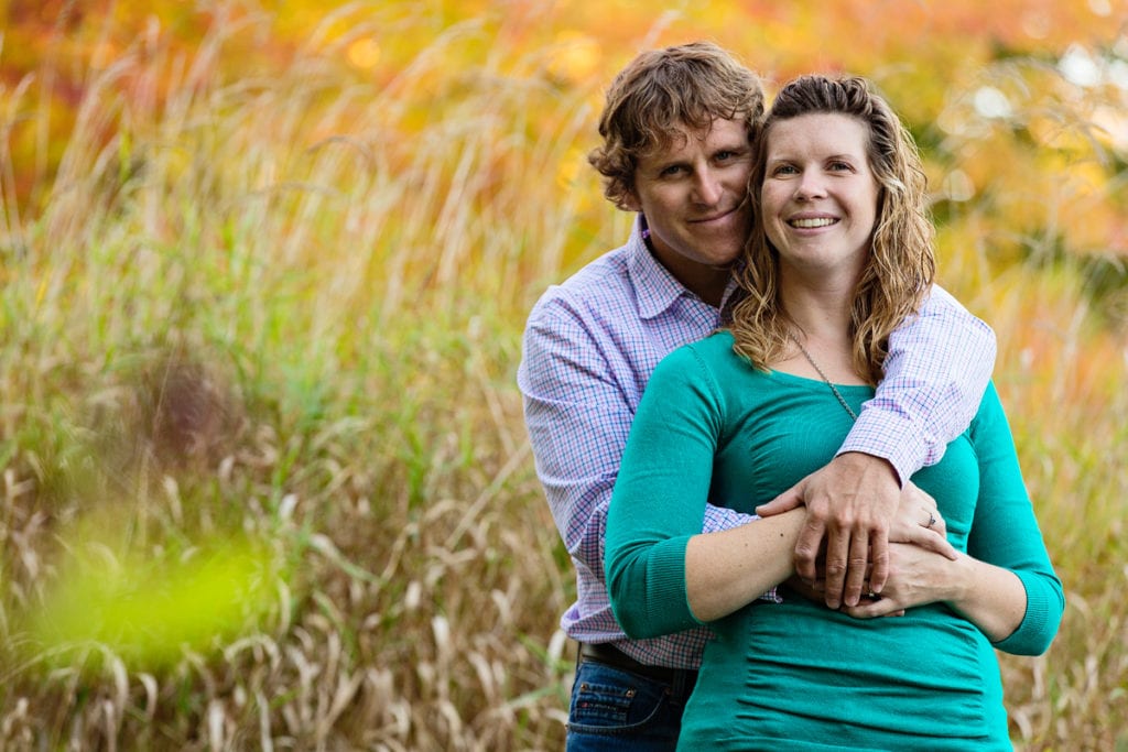 man embracing fiancee in tall grass field in fall rural engagement session