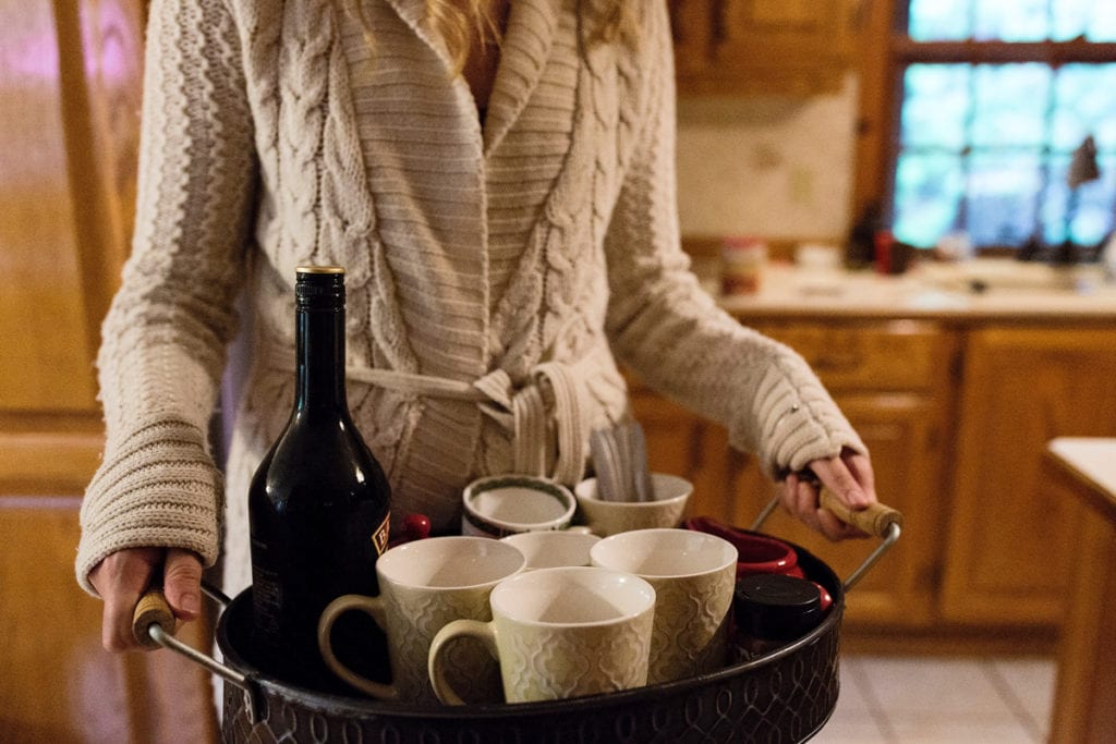 young woman in cozy cable knit sweater serving coffee and baileys with mugs on serving tray