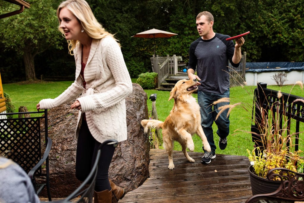 young couple playing with dog and joining family on patio in casual family session