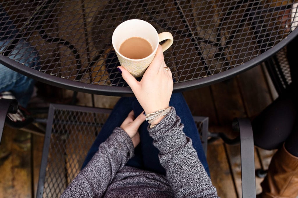 bracelet wearing young woman holding coffee at outdoor patio table