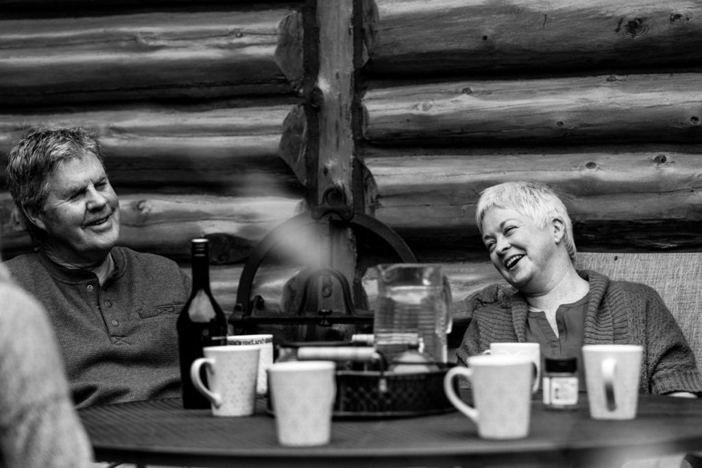mom and dad laughing over coffee on outdoor patio of log cabin