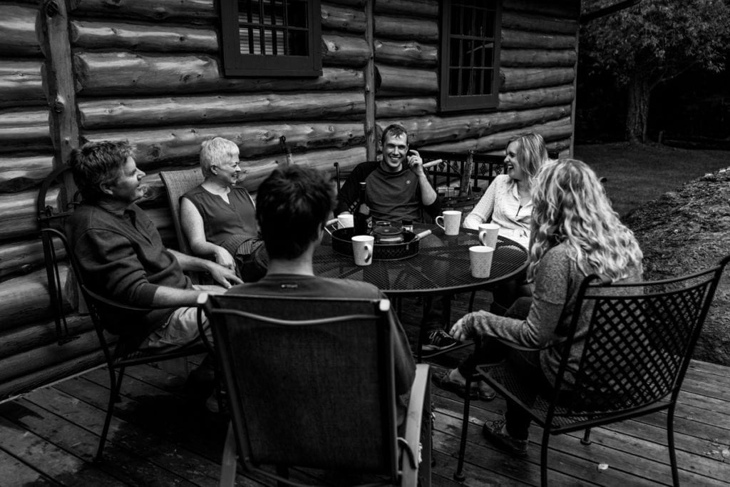 family sharing laughs and coffee at outdoor patio table of log cabin during Ontario Casual Family Portraits