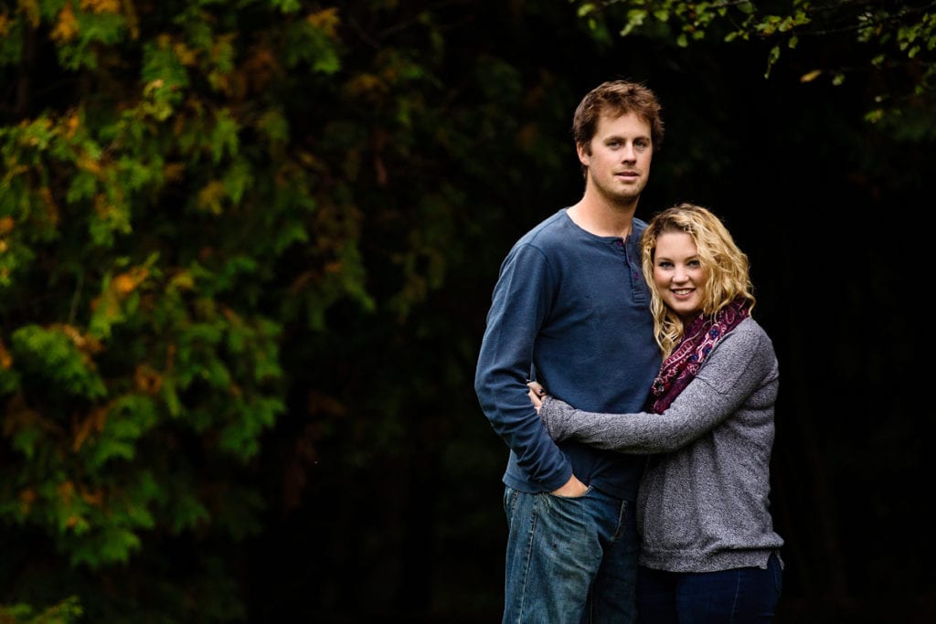 young smiling couple in front of dark green leafy background