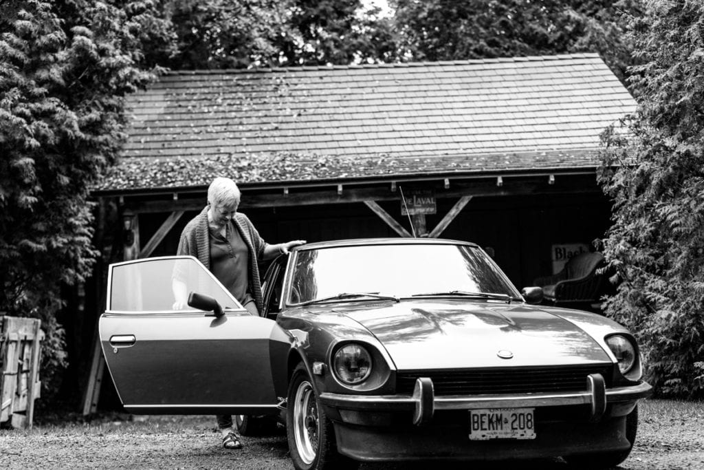 woman getting into passenger side of classic car in front of country garage
