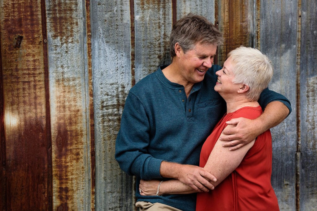 woman in bright red blouse and man in blue sweater against rusting tin shed