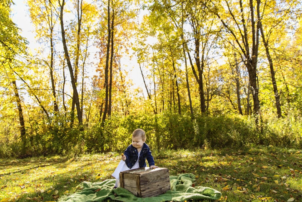 baby girl in navy blue cardigan and dress playing with wooden crate in sunlit nature scene