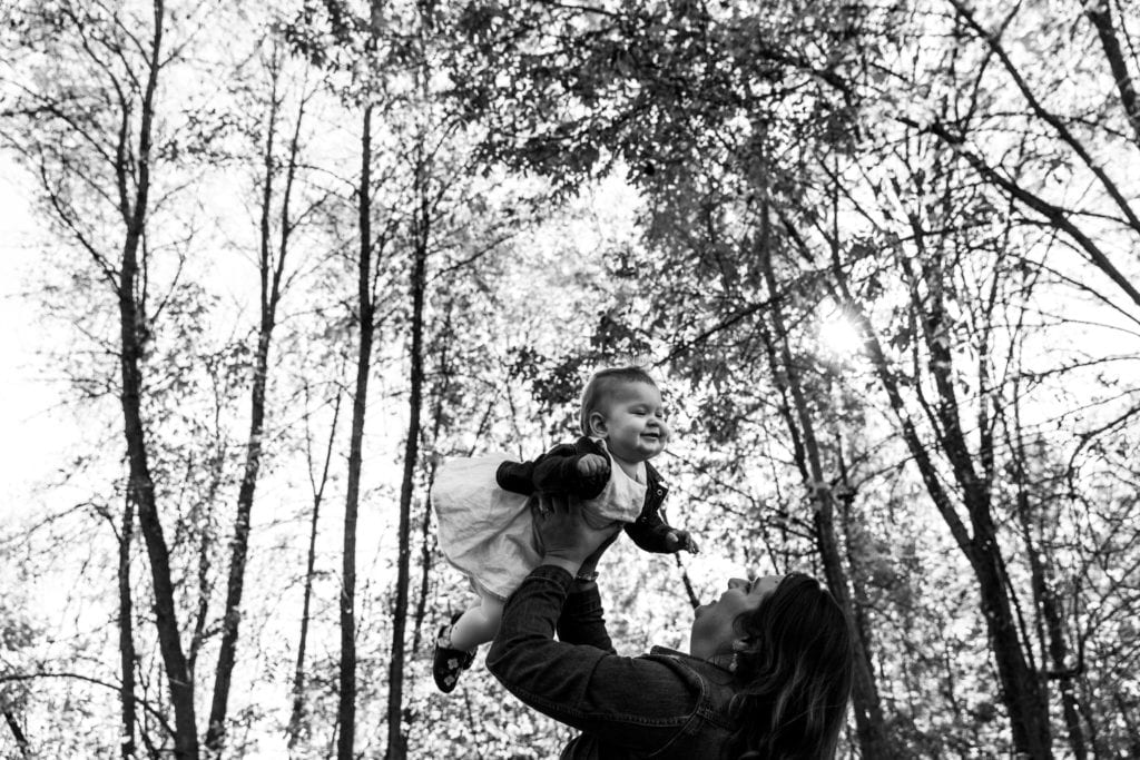 mom holding smiling baby girl up in the air in non-traditional family portrait