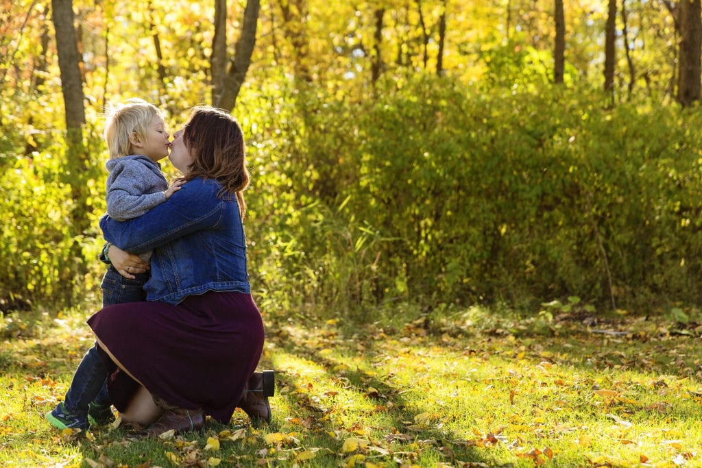 mom and young son sharing a kiss in sunlit forest
