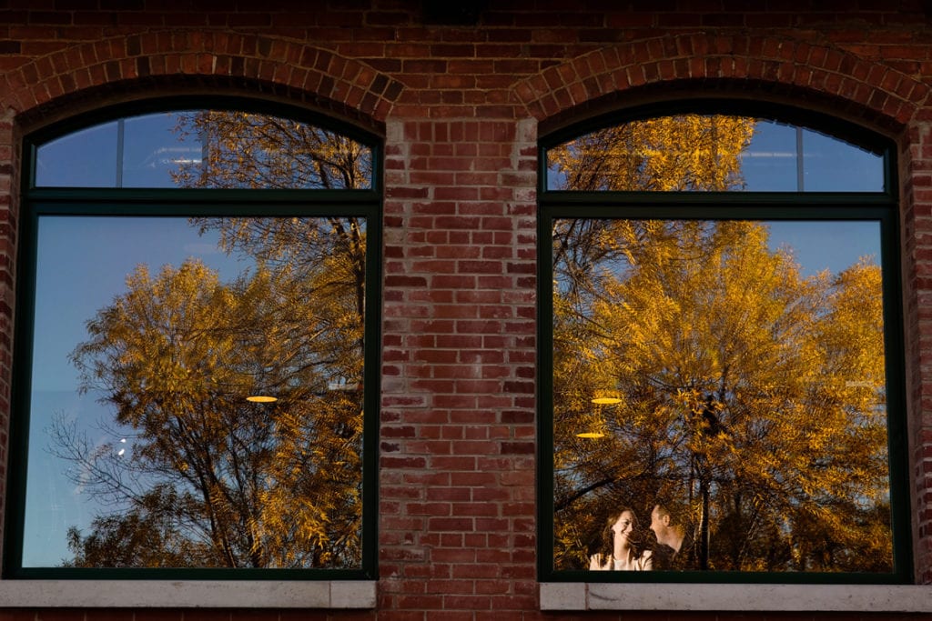 unique shot of couple in coffee shop window with fall tree reflection during Autumnal Cornwall engagement session