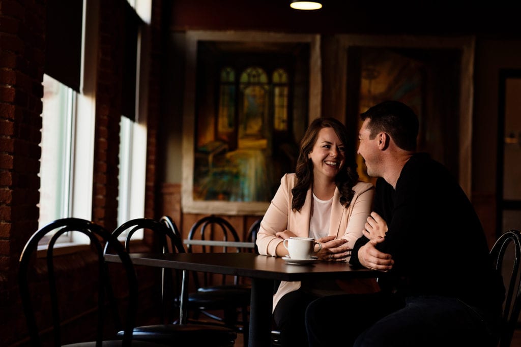 couple laughing and smiling in coffee shop during Cornwall engagement session