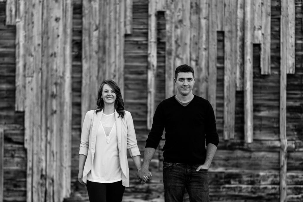couple holding hands in front of rustic building in fall engagement shoot