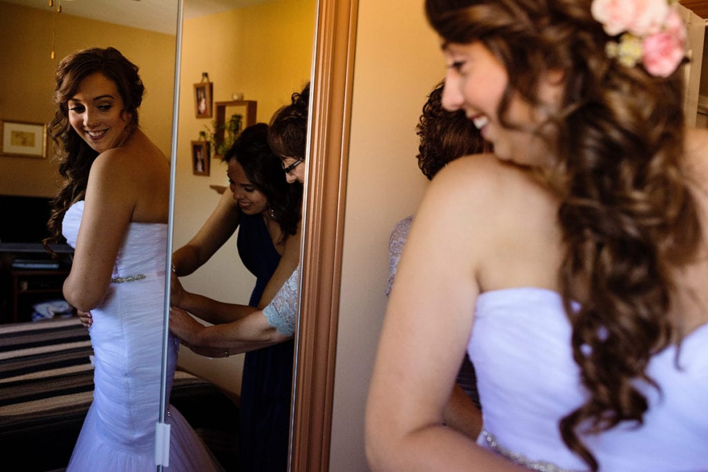 bride gets help with dress from mom and sister