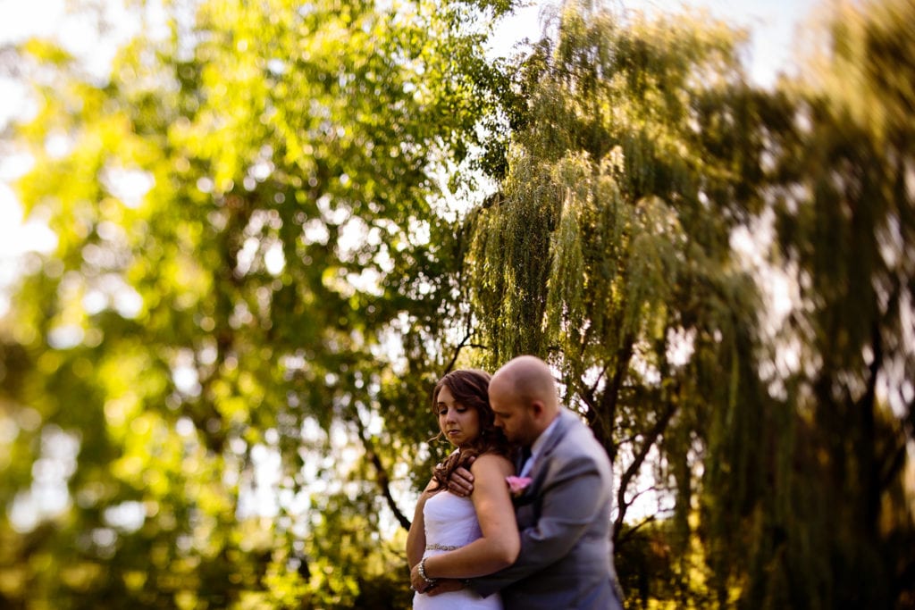 groom holds bride and nuzzles her neck in park