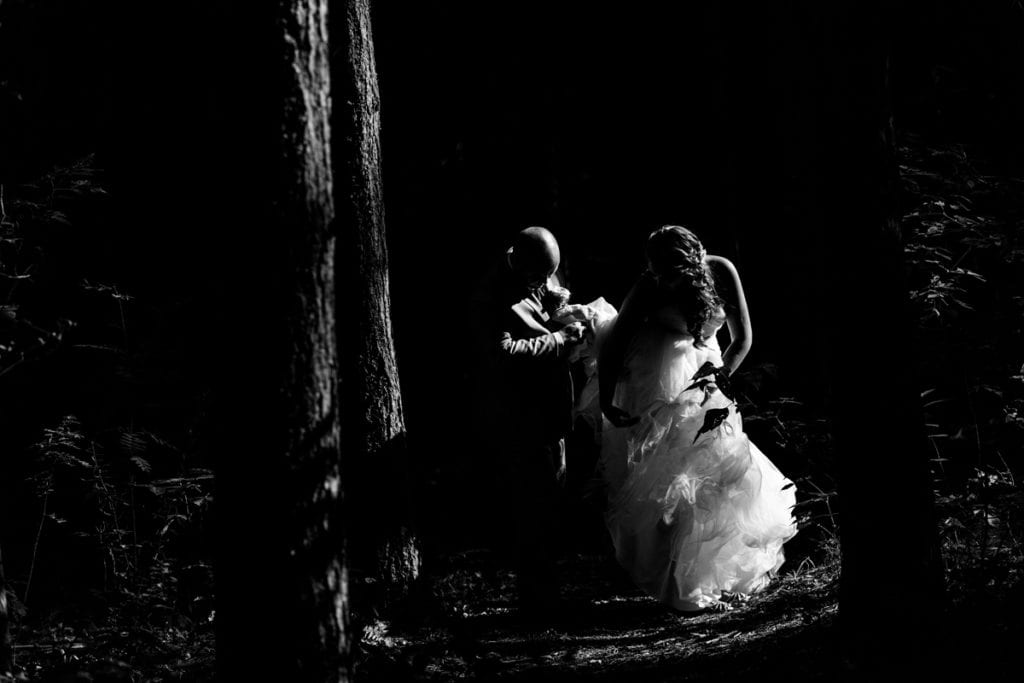 groom helps bride with fit and flare gown in the forest