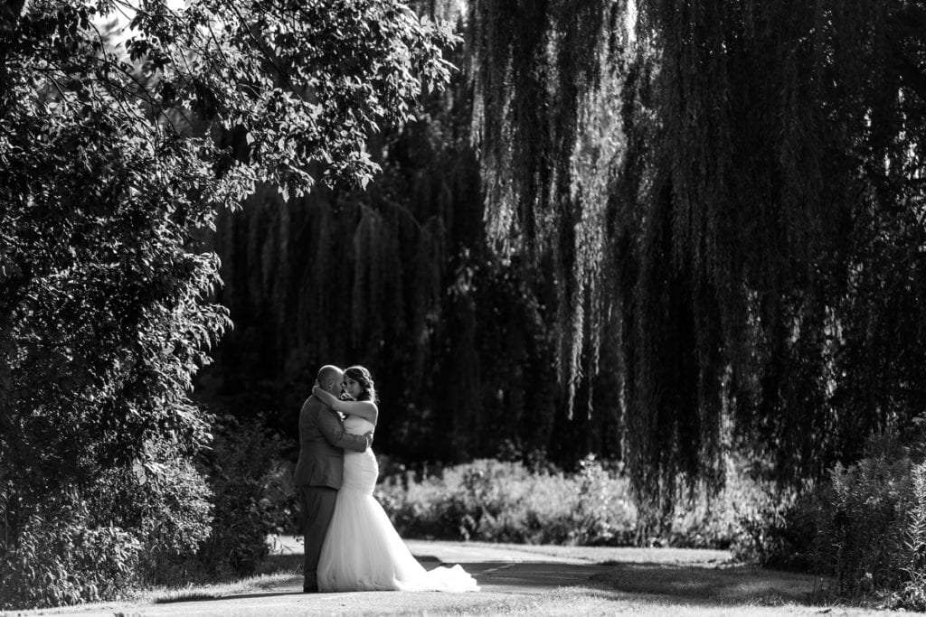 bride and groom hug under willow trees on bicycle path