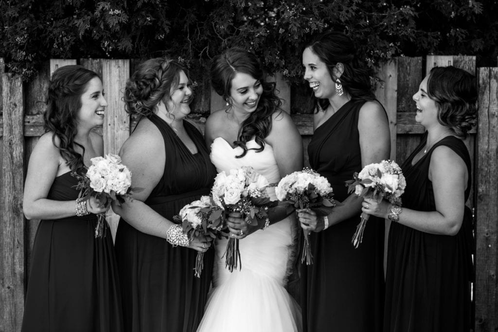 bride laughs with bridesmaids in front of fence