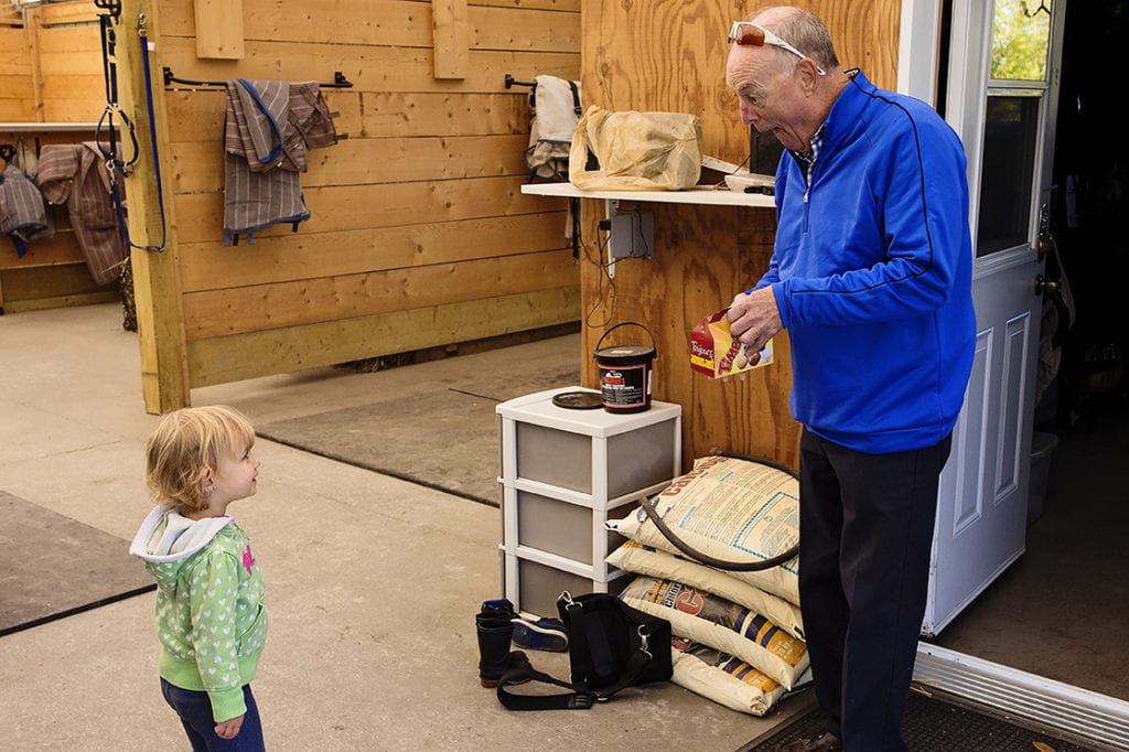 grandpa making funny faces at granddaughter while holding box of doughnuts