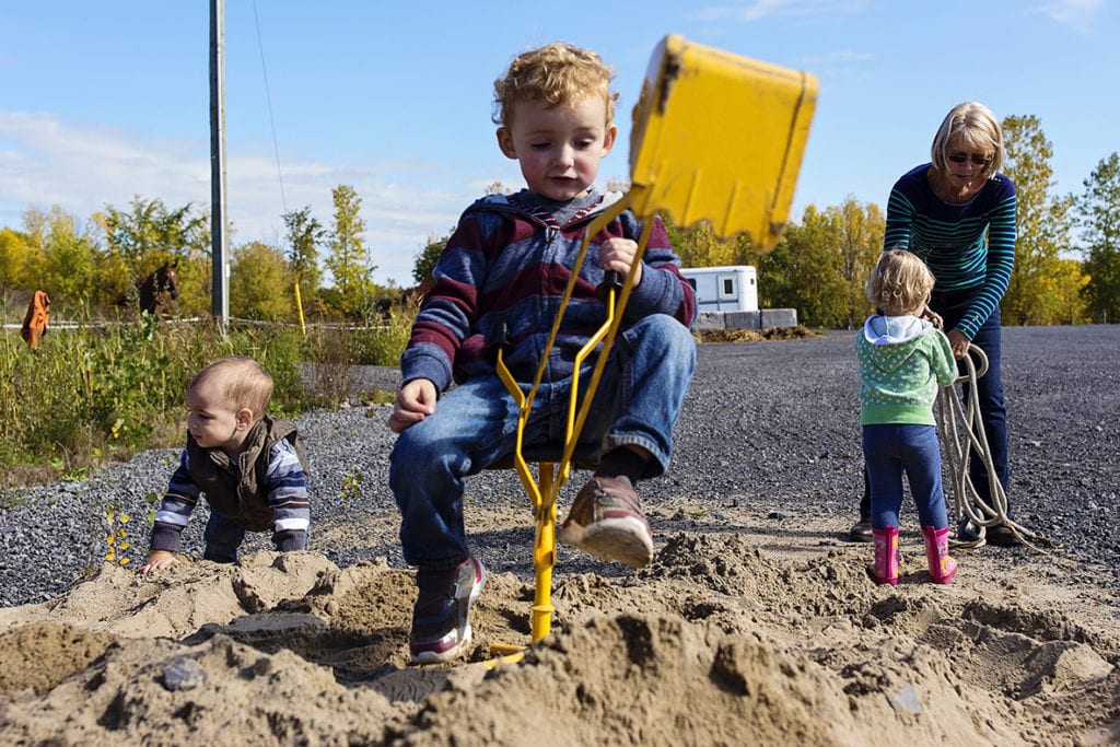 little kids playing in sand and boy using shovel
