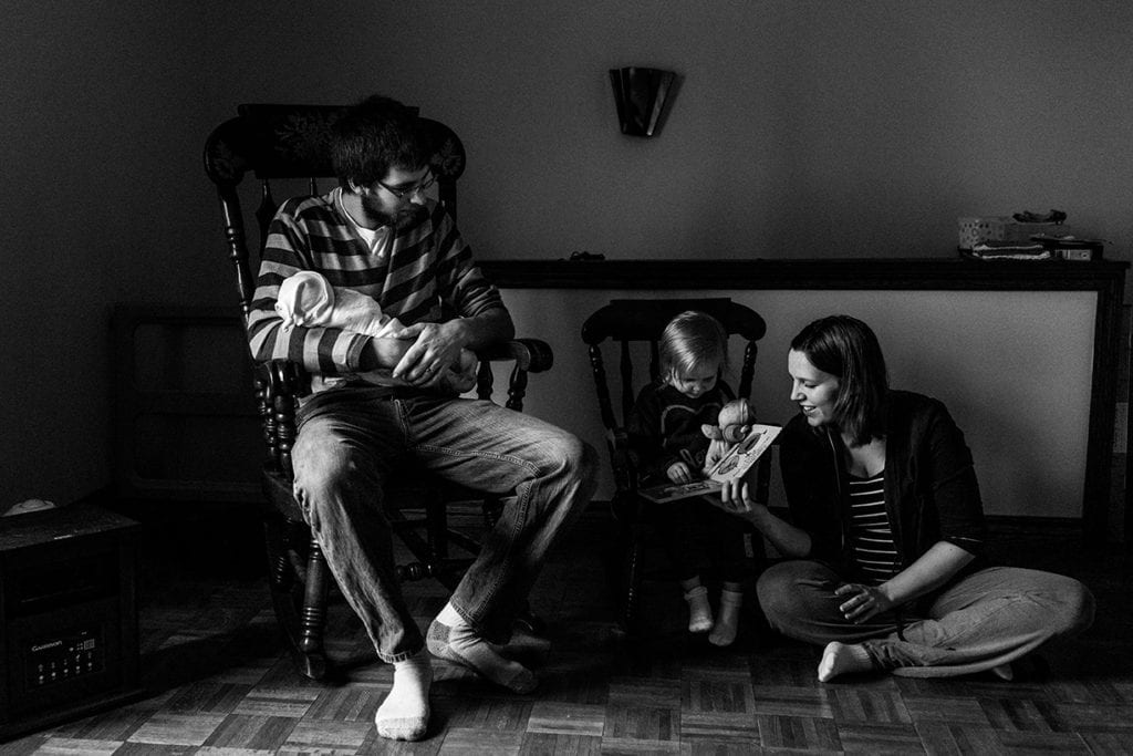 family reading book in rocking chairs during session with Ottawa family photographer