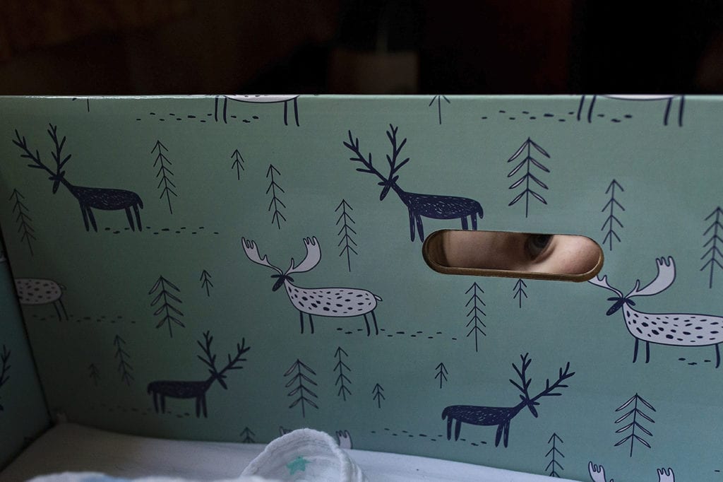 sister peeking through handle hole of brother's baby box