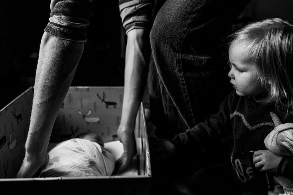 daughter looking on as father picks up newborn