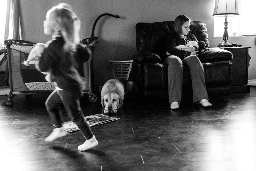 daughter running past breastfeeding mother and dog