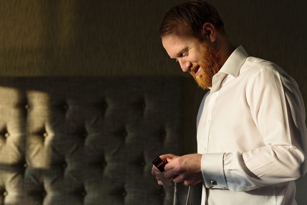 groomsman removes tag from tie during groom prep at Christchurch Habour Hotel & Spa