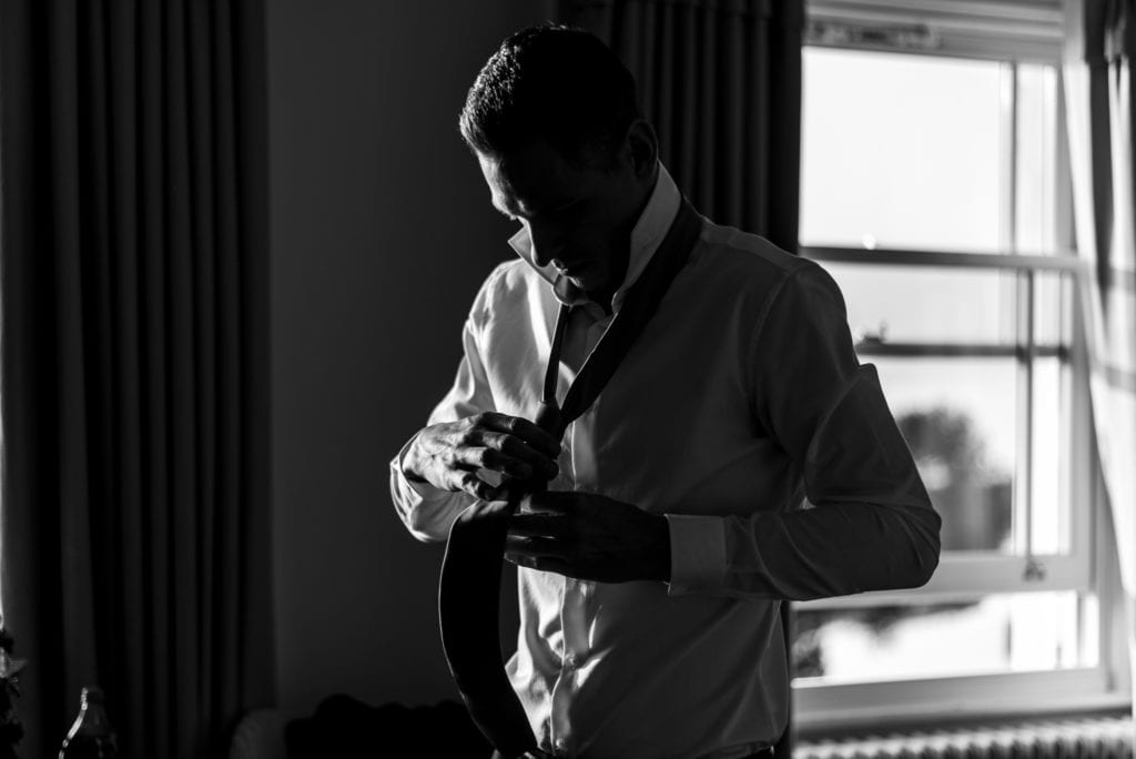 groom holds out tie with tying it during groom prep at Christchurch Habour Hotel & Spa