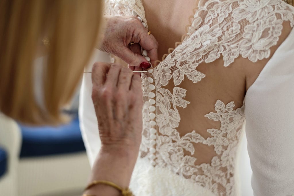 mother of the bride uses crochet hook to fasten buttons on chic New Forest wedding gown during bridal prep at Christchurch Habour Hotel & Spa