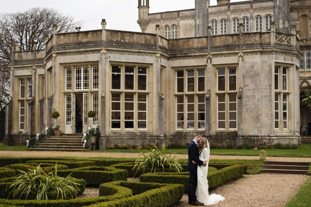 groom embraces bride on pathway after chic New Forest wedding ceremony at Highcliffe Castle