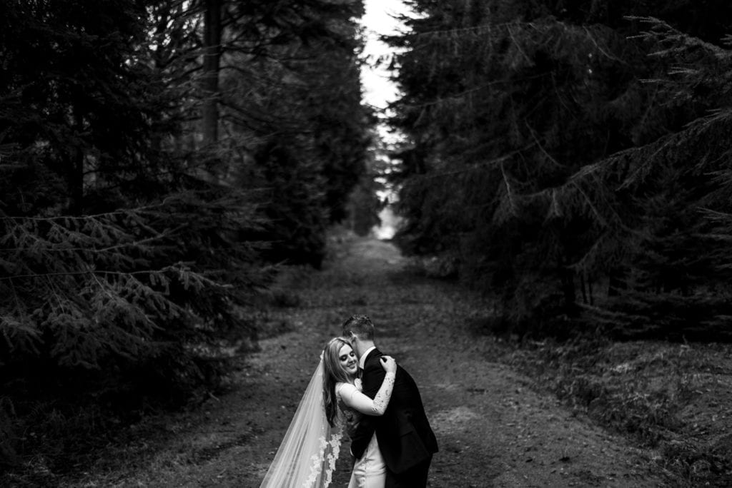 groom pulls bride close while they stand in path cleared between pines on Rhinefield Ornamental Drive during New Forest wedding portraits