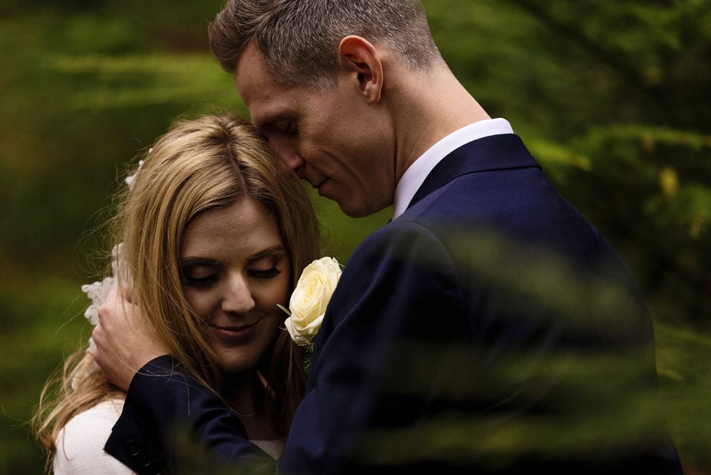 groom places hand on bride's neck and nuzzles her amongst pines on Rhinefield Ornamental Drive during New Forest wedding portraits