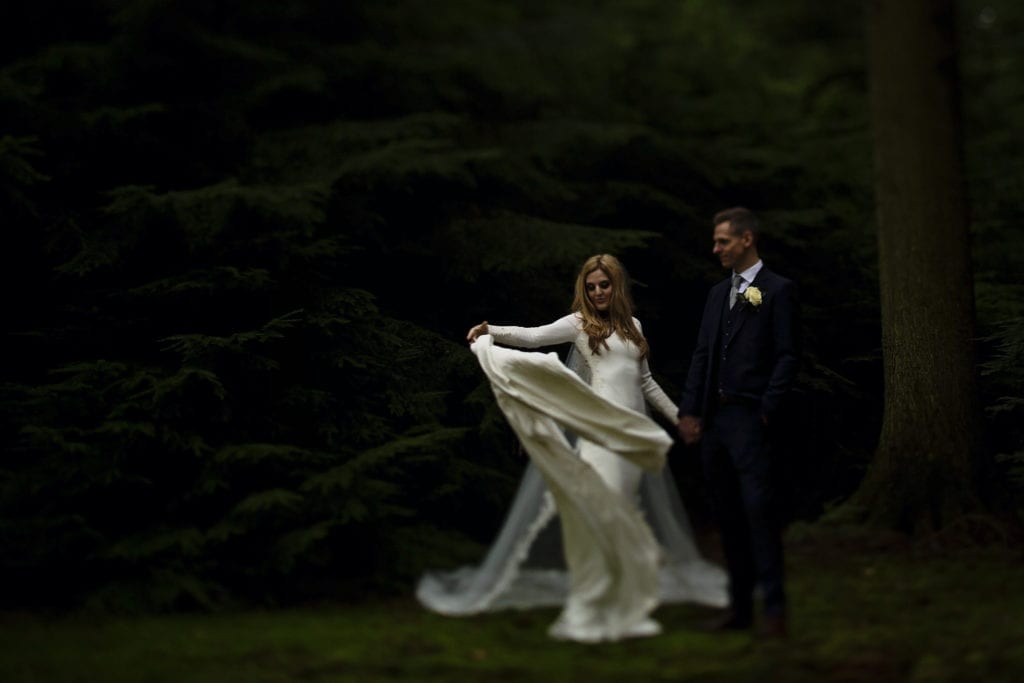 bride flings dress dramatically in pine grove on Rhinefield Ornamental Drive during New Forest wedding portraits