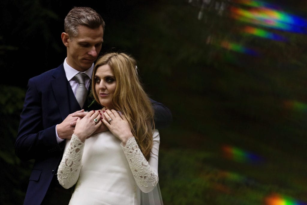 groom touches bride's shoulder while standing amongst trees on Rhinefield Ornamental Drive during New Forest wedding portraits