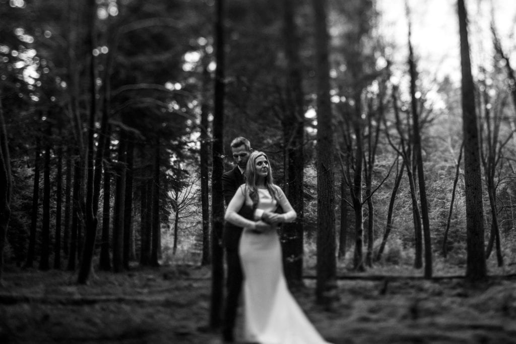 bride stands in front of groom while he wraps arms around her amongst trees on Rhinefield Ornamental Drive during New Forest wedding portraits