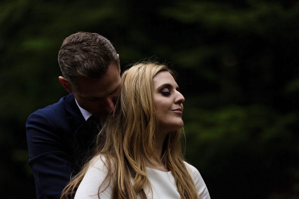 groom bends to kiss bride's neck amongst trees on Rhinefield Ornamental Drive during New Forest wedding portraits