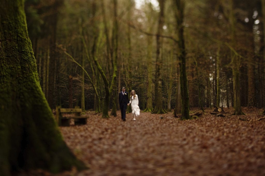 Bride holds dress and groom's hand while walking through the leaves on Rhinefield Ornamental Drive during New Forest wedding portraits