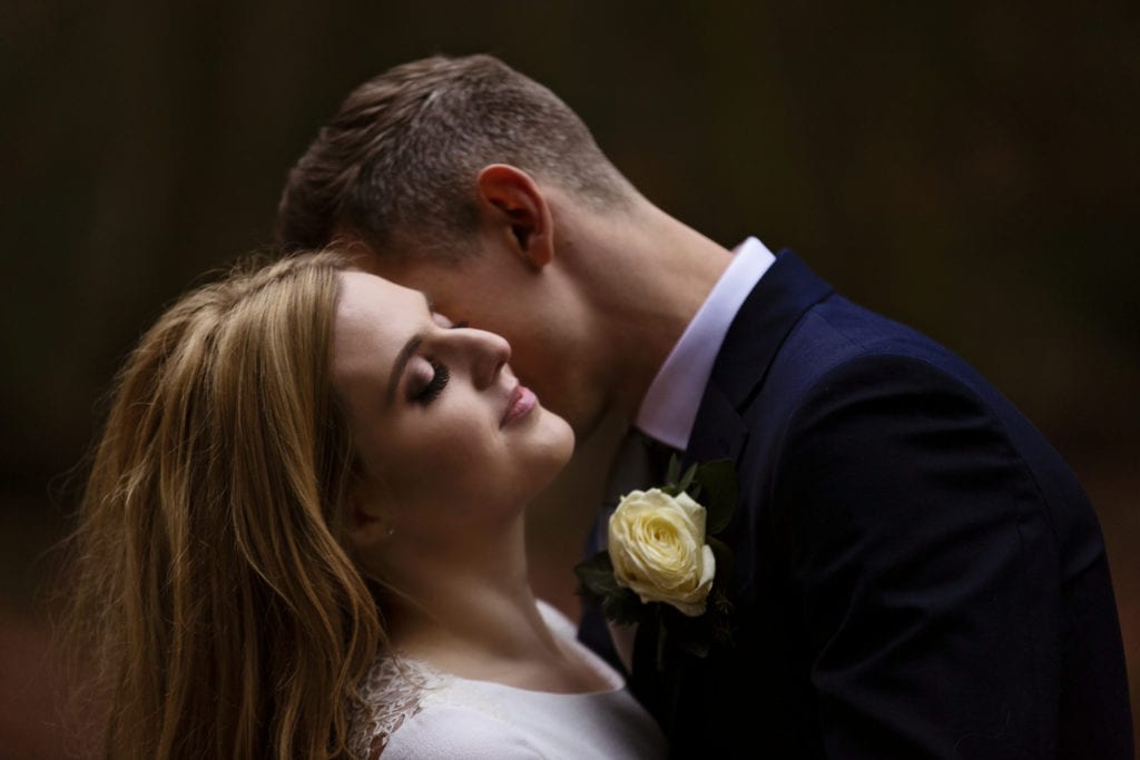 bride tilts head back while groom nuzzles her neck in forest on Rhinefield Ornamental Drive during chic New Forest wedding portraits