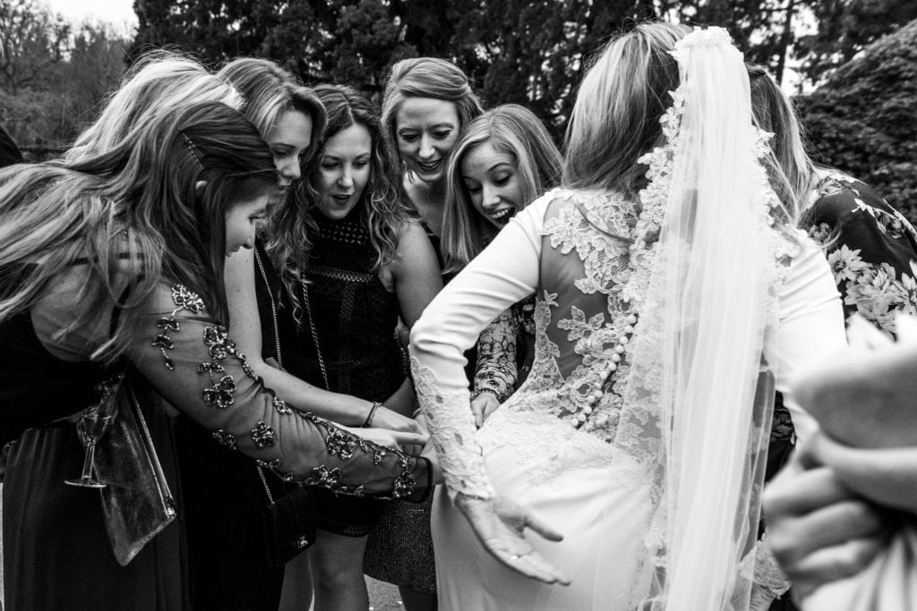women gather round bride and look surprised while touching her bum during wedding reception at Rhinefield House