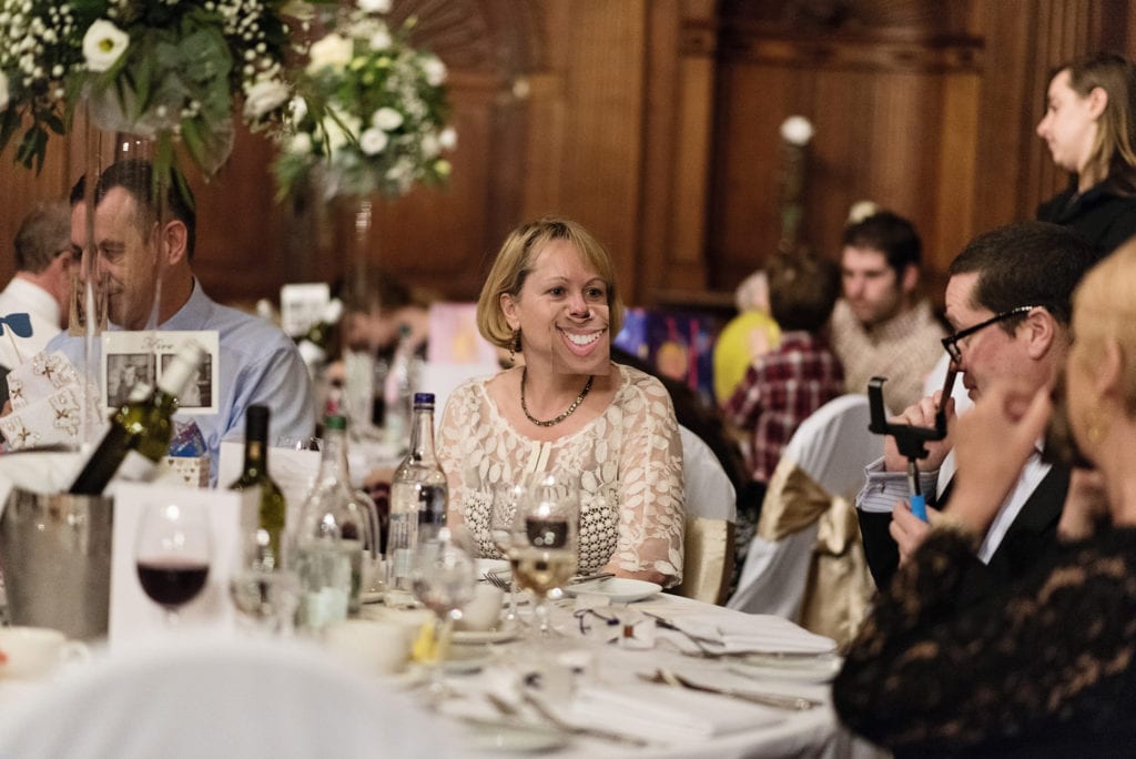 woman in formal dress wears cardboard cutout on her face of big toothy grin during wedding reception at Rhinefield House