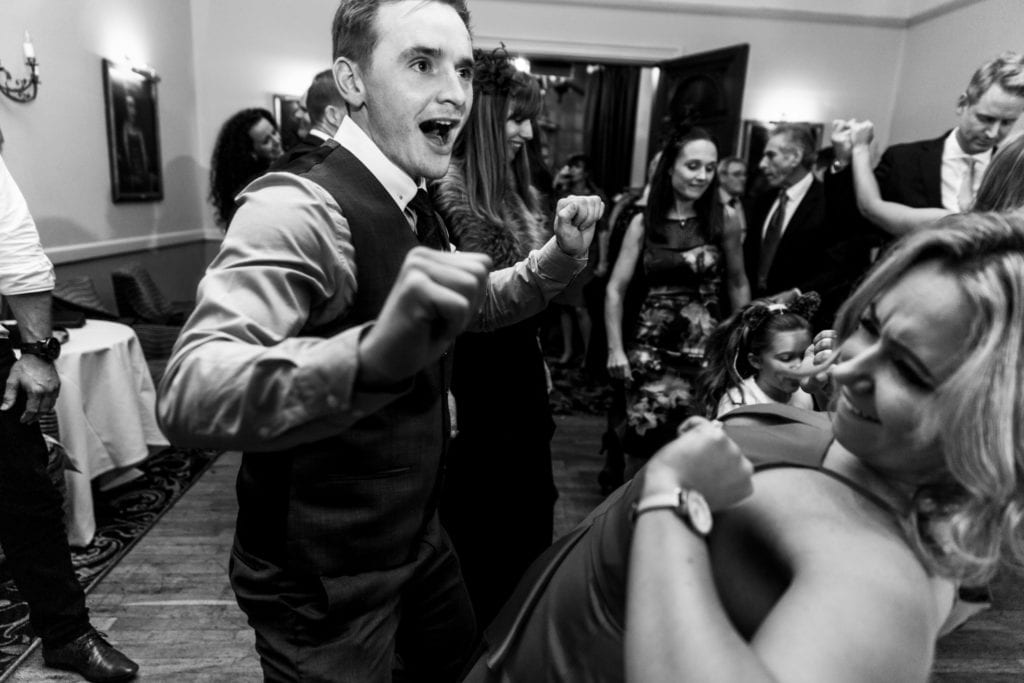 Man dances enthusiastically with woman who bends backwards during wedding reception at Rhinefield House