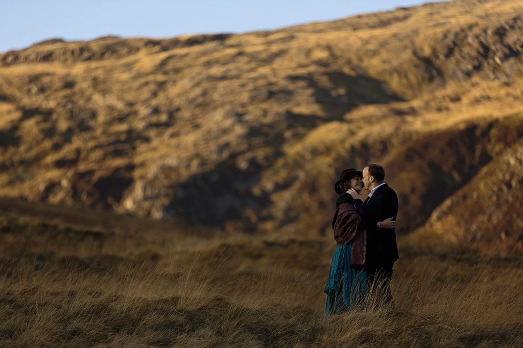 woman wearing shawl leans in close to husband among golden grass during Snowdonia portrait session